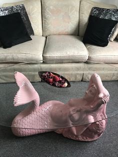 a pink mermaid statue sitting on top of a glass table next to a white couch