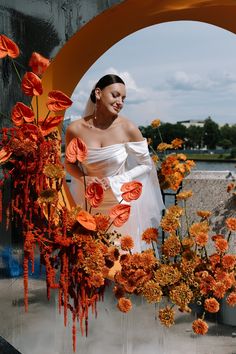 a woman in a white dress standing next to flowers and an archway with orange decorations