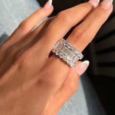 a woman's hand holding an engagement ring with two baguettes on it