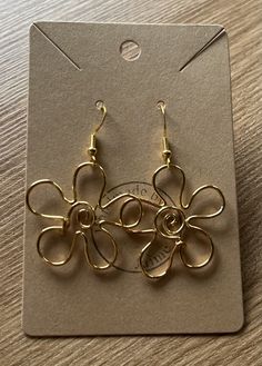 two pairs of gold toned metal earrings on top of a wooden table next to a card