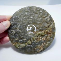 a person holding a piece of jade with swirls on it's side and a circular object in the middle