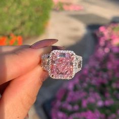 a woman's hand holding an engagement ring with a pink diamond in the center