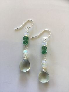 I love the colour combination of these stones. Heart shape smooth green amethyst, with flashing rondelle moonstones and untreated, natural emeralds. The wiring is sterling silver. The ear wires are also sterling silver but I can change them to surgical silver ones. Also, white gold is always an option however I would have to order them in. ABOUT SHIPPING- Shipping within Canada is crazy expensive. If there is any overage I will refund. I'm very limited in adding different cost of shipping betwee Green Moonstone Jewelry Gift, Green Moonstone Jewelry With Natural Stones, Silver Rondelle Gemstones For Jewelry Making, Green Moonstone Round Jewelry, Green Moonstone Jewelry For Healing, Green Sterling Silver Crystal Earrings, Green Amethyst Gemstone Earrings, Silver Briolette Jewelry For May Birthstone, Handmade Silver Briolette Gemstones