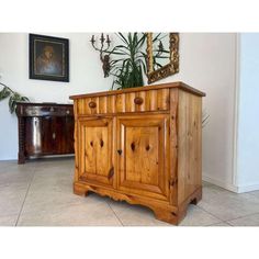 a wooden cabinet sitting on top of a tile floor next to a potted plant