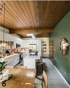 a kitchen with green walls and wood ceilinging next to a wooden dining room table