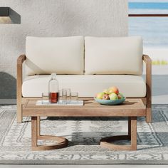 a coffee table with fruit on it in front of a white couch and window overlooking the ocean