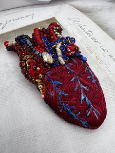 an embroidered heart is sitting on top of a piece of fabric with beads and chains