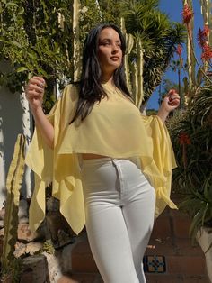 a woman in white jeans and a yellow top posing for the camera with cactus trees behind her