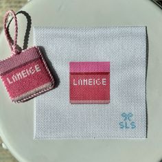 a white plate topped with a pink tag next to a red and white cross stitch bag