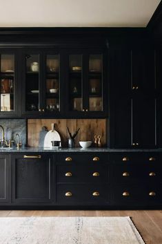 a kitchen with black cabinets and gold pulls on the doors, along with an area rug