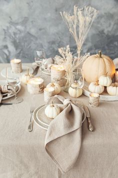 the table is set with white pumpkins and silverware, candles and linen napkins