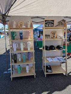 two wooden shelves with cups and mugs on them under a tent at an outdoor market