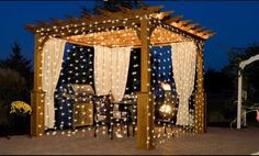 an outdoor gazebo with lights on it and curtains over the top, sitting outside at night