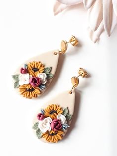 two sunflowers and leaves are hanging from the back of white earring earrings