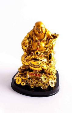 a golden buddha statue sitting on top of a black base with gold coins around it