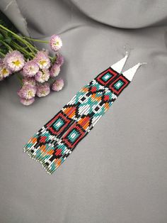 a beaded bracelet next to flowers on a gray cloth with white and red beads