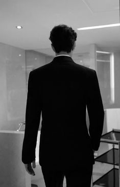 a man in a suit is looking out the window at an office building with glass partitions