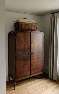 a wooden cabinet sitting in the corner of a room with a basket on top of it