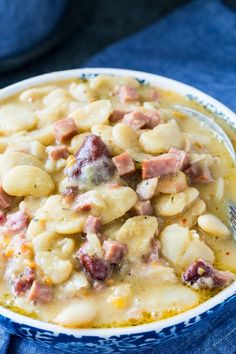 a bowl filled with pasta and ham on top of a blue cloth next to a spoon