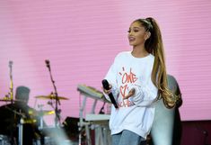 a woman holding a microphone in her right hand and standing next to a drum set