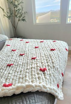 a white crocheted blanket with red hearts on it sitting on top of a bed