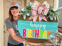 a woman holding a happy birthday sign in front of a door with flowers on it