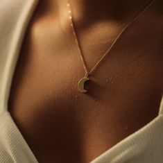 a woman wearing a gold necklace with a crescent pendant on it's neck,