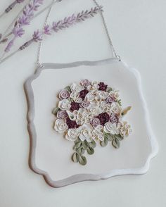 a white plate with flowers on it and some lavenders in the background, hanging from a chain