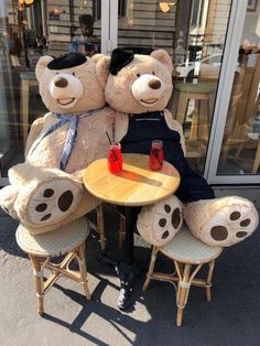 two large teddy bears sitting at a table with drinks on it in front of a store