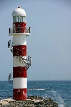 a red and white lighthouse sitting on top of a rocky cliff next to the ocean