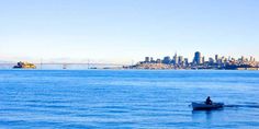 a person in a small boat on the water with a city in the back ground