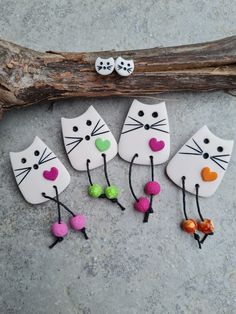 four white cat magnets with hearts on them sitting next to a piece of drift wood