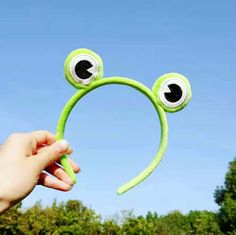 a hand holding up a green headband with eyes