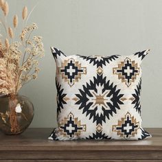 a black and white pillow sitting on top of a wooden table next to a vase