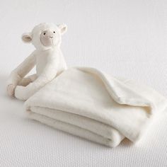 a white stuffed animal sitting on top of a pile of folded blankets with one eye closed