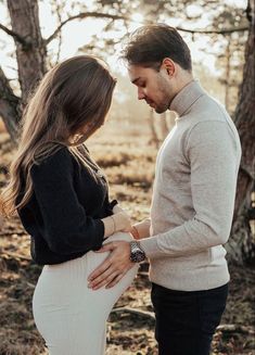 a pregnant woman standing next to a man in the woods with her hands on her stomach