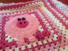 a crocheted blanket with a pink pig on it's face and black eyes