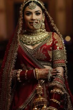 a woman in a red and gold bridal outfit with jewelry on her head,