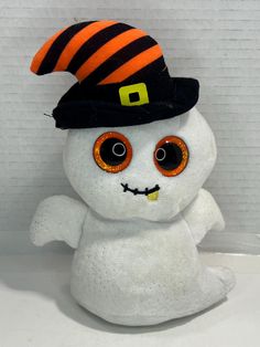 a white stuffed animal with orange eyes and a black hat