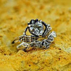 two silver rings sitting on top of a yellow rock covered in dirt and sand, with a diamond center surrounded by leaves