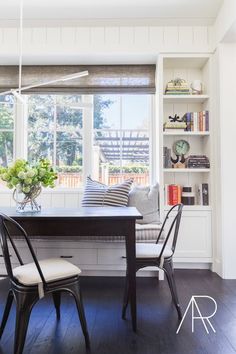 a dining room table with two chairs and a bench in front of a window filled with books