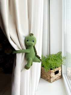 a crocheted green stuffed animal hanging on the side of a curtain