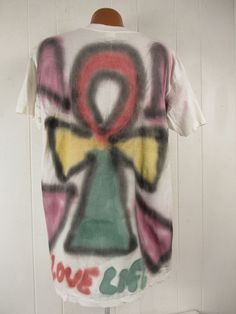 "Vintage 1990s primitive outsider or folk art style t shirt. Made of white cotton with 2 sided air brushed graphics. Has large portrait on the front and symbol on back. Reads: Come back Jesus Love Life. Signed: Loren A. Evans 91. Size extra large. Actual measurements are: 46\" around the chest 46\" around the waist 22\" shoulder seam to shoulder seam 32\" overall length In excellent condition." Bohemian Cotton T-shirt For Streetwear, Unisex Festival T-shirt With Screen Print, Vintage Multicolor Graffiti Print T-shirt, Vintage Hand Printed Short Sleeve T-shirt, Vintage Hand-printed Short Sleeve T-shirt, Summer Unisex Hand Printed T-shirt, Bohemian Short Sleeve T-shirt For Streetwear, Hippie Style Screen Print T-shirt For Festival, Cotton Artwork T-shirt With Short Sleeves