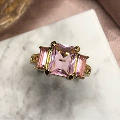 a pink and yellow ring sitting on top of a white marble table next to a gold plate