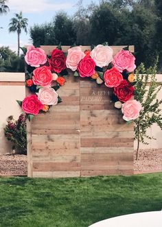 a wooden sign with flowers on it in front of some grass and palm tree's