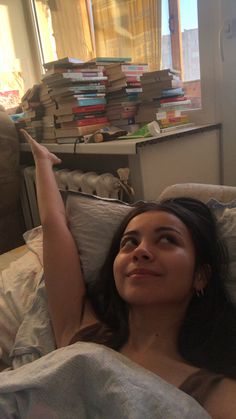 a woman laying in bed with lots of books on the wall behind her and she is smiling