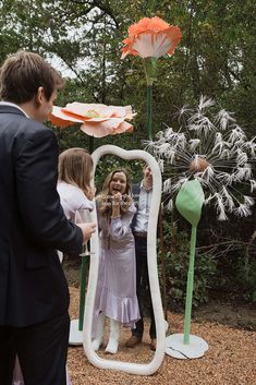 a woman standing in front of a large mirror with flowers on it and people looking at her