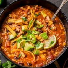 a bowl of chili soup with avocado and cilantro on the side