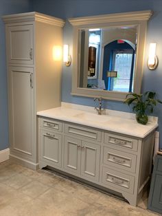 a bathroom with blue walls and white cabinetry has a large mirror on the wall