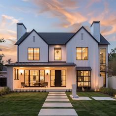 a large white house with lots of windows and grass in the front yard at dusk